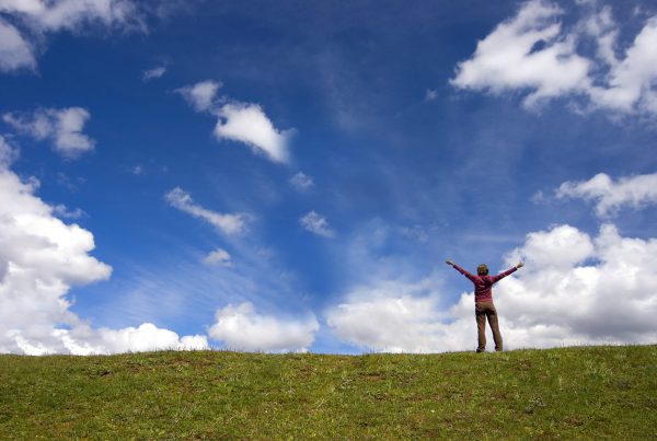 A Person standing in an open field with arms open as they perform Breathwork to Expand & Raise Consciousness